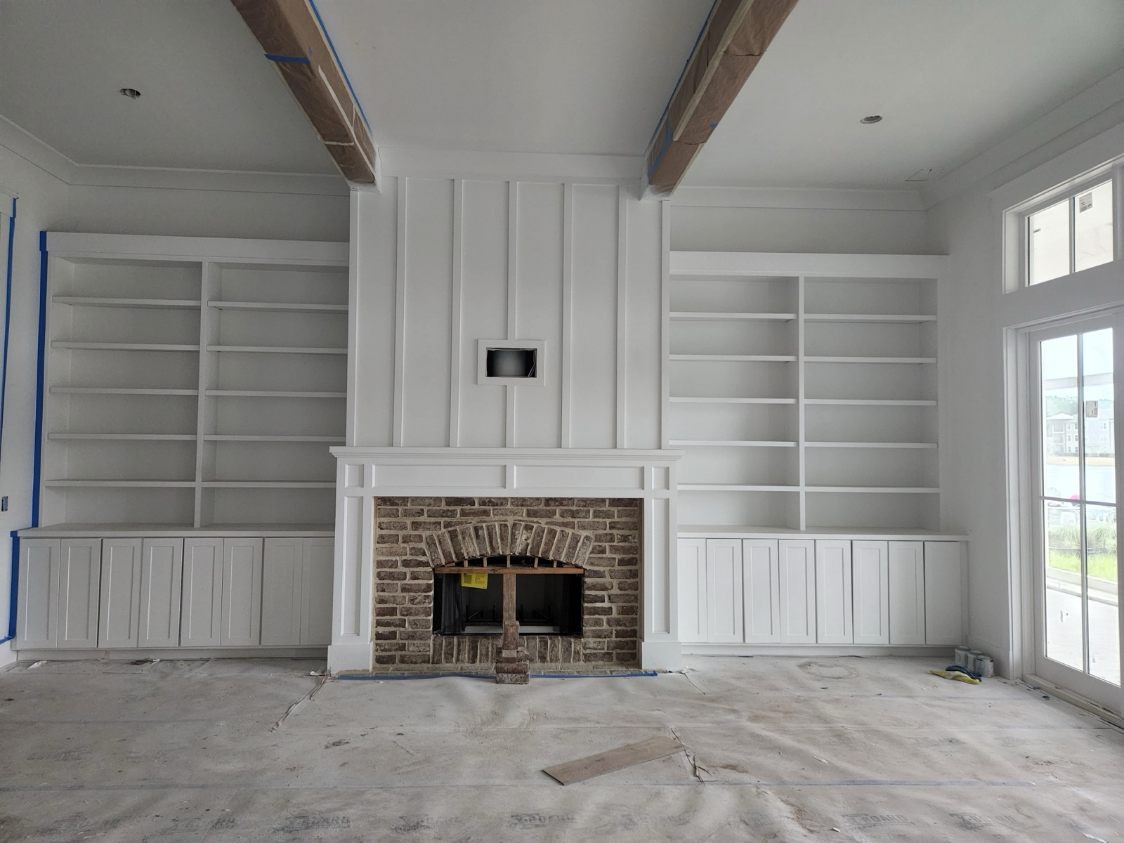 Custom millwork with wood beams and built in bookshelves flanking a brick fireplace during construction